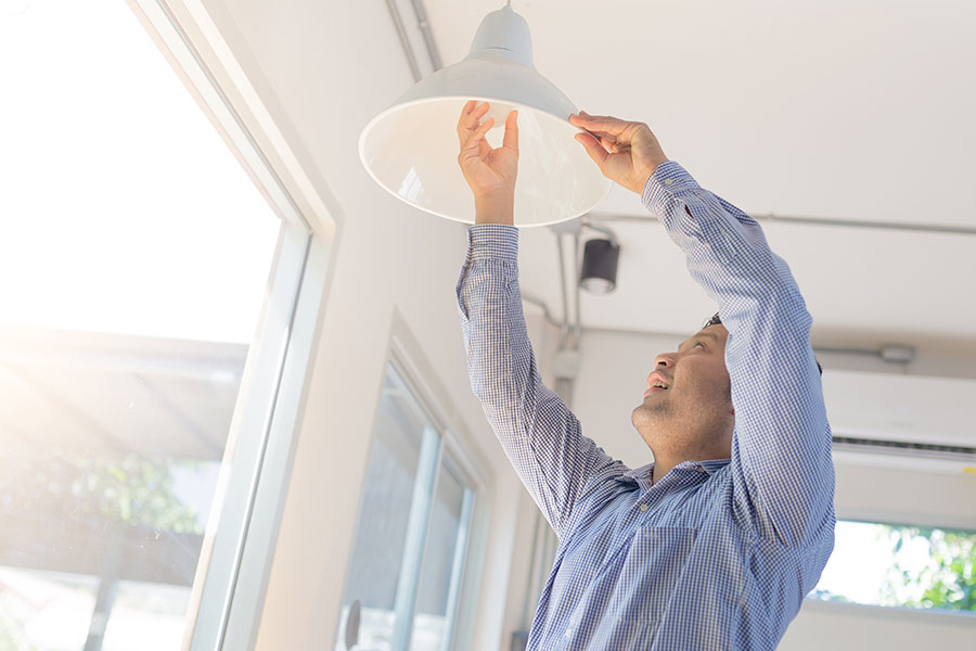 Asian man changing a light bulb at home and installing an energy efficient LED light bulb
