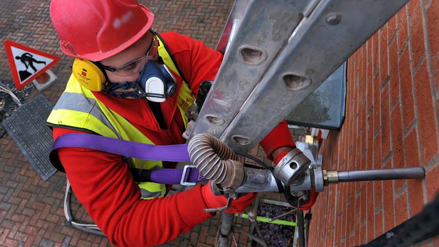 Man carrying out cavity wall insulation work on a house from the outside