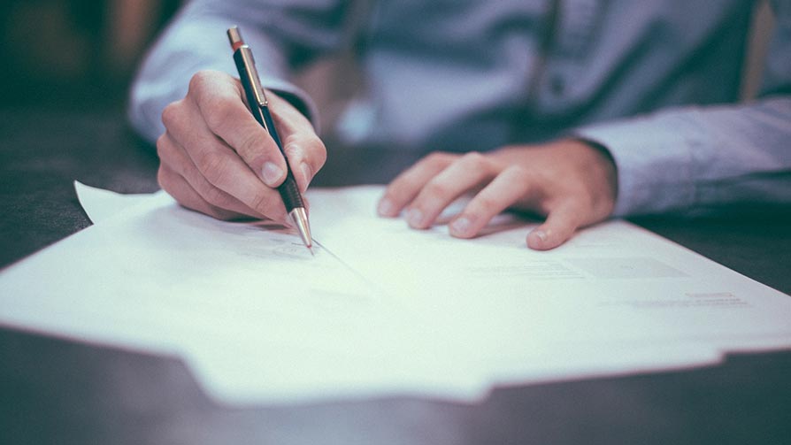 Person writing at a desk with certificates, inspection letters and paperwork